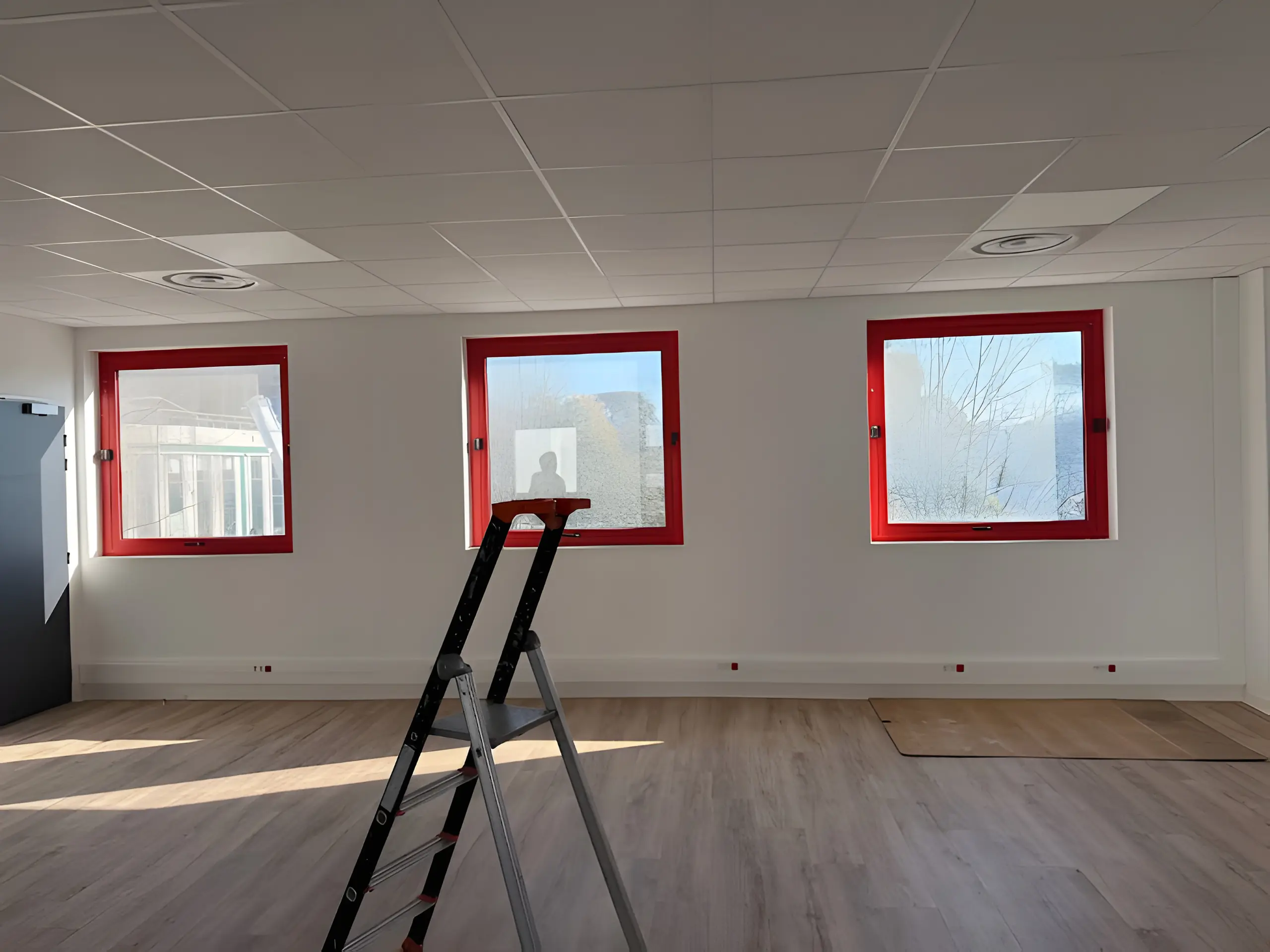 Plateau de bureaux vide avec trois fenêtres à cadre rouge et un escabeau